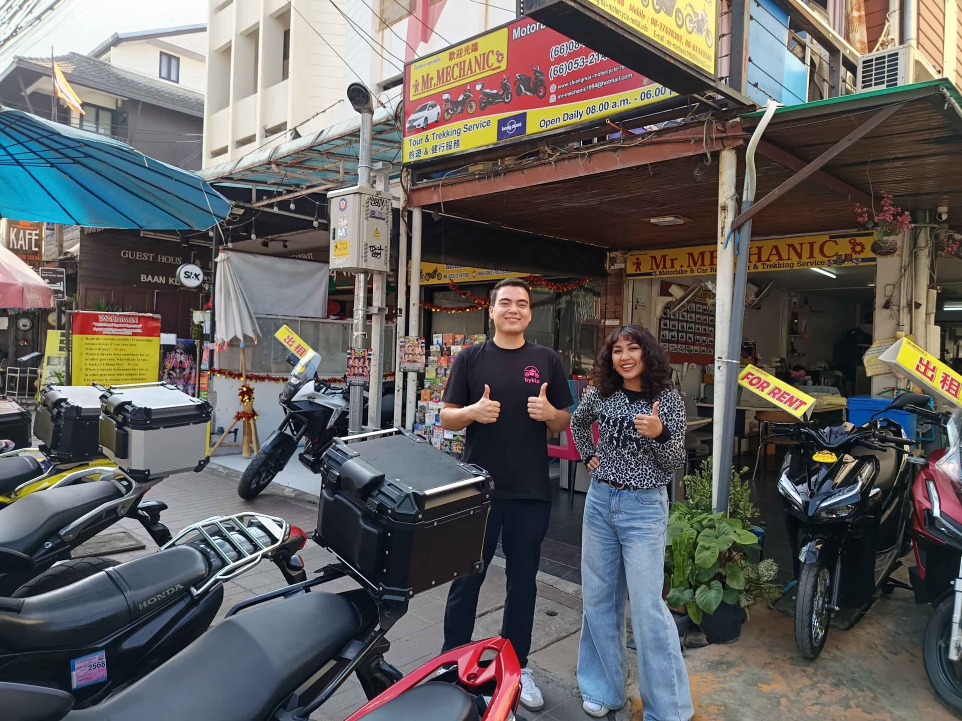 Thai Man and Woman standing outside motorbike rental shop showing thumbs up