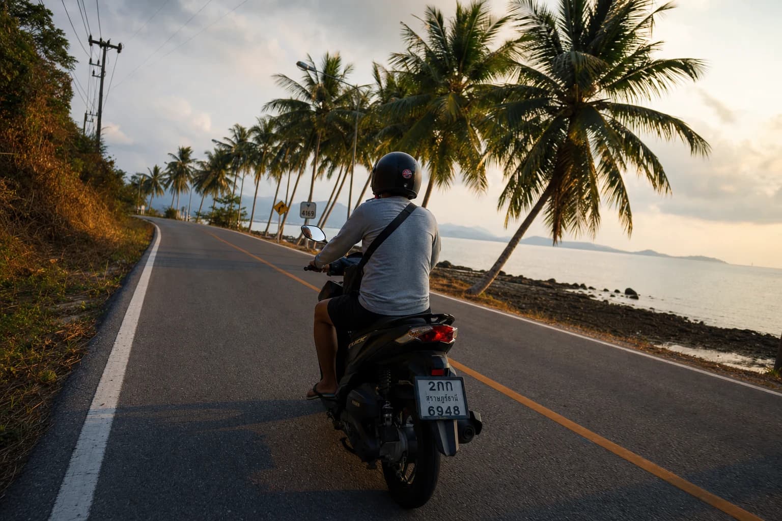 Honda Click 125cc di Jalan Lingkaran Laluan 4169 sekeliling Koh Samui, dengan pantai teluk dan bahu jalan berbaris pokok kelapa di latar belakang