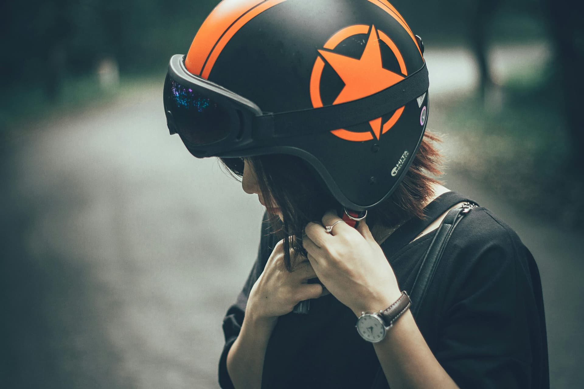Motorcyclist adjusting a black and orange helmet with a star emblem on a quiet road