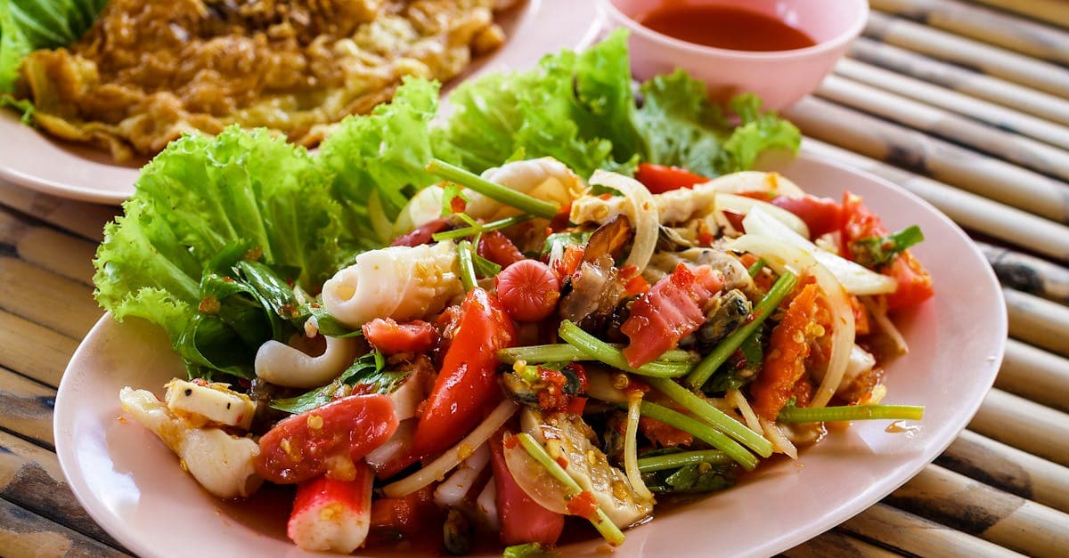Authentic Thai seafood salad with fresh vegetables and herbs served on a pink plate.
