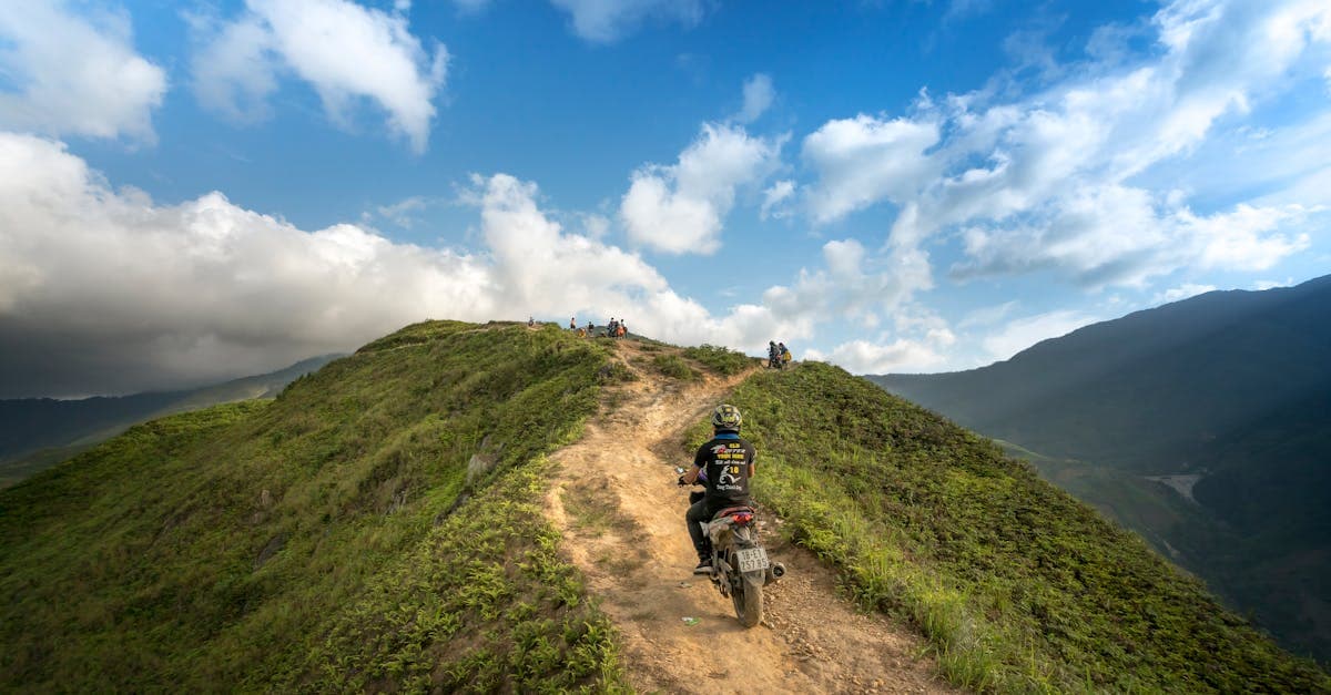 A motorcyclist travels along a rugged mountain path under a vibrant summer sky, perfect for adventure enthusiasts.