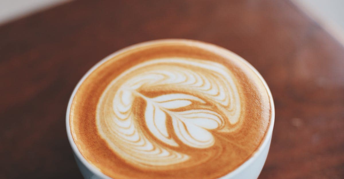 A beautifully crafted latte with intricate latte art inside a white ceramic cup on a wooden table.