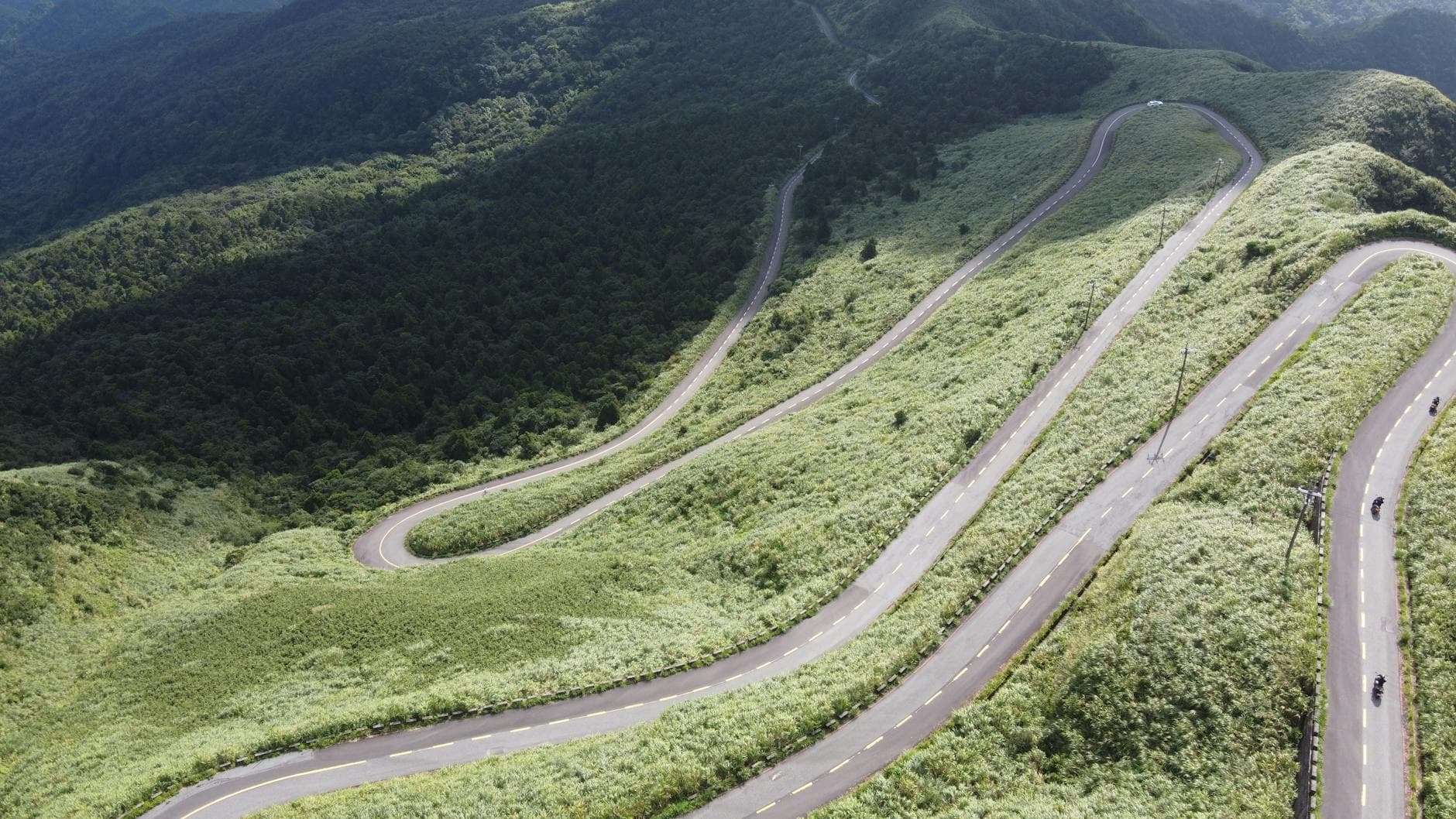 Aerial view of a winding mountain road surrounded by lush green forest in Ruifang District, Taiwan.