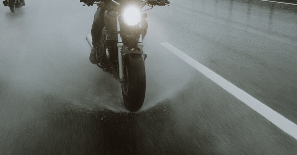 Motorcyclists navigate a wet highway at night, splashing water during their ride.