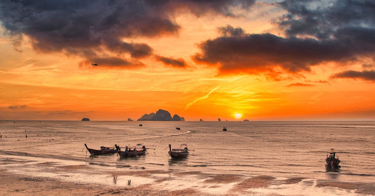 Golden sunset over Krabi beach with traditional boats and dramatic clouds.