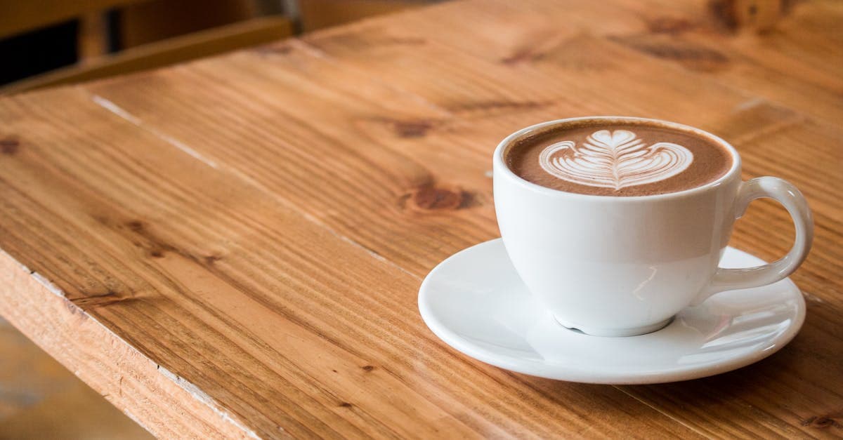 Close-up of a white cup of latte with artistic foam on a rustic wooden table.