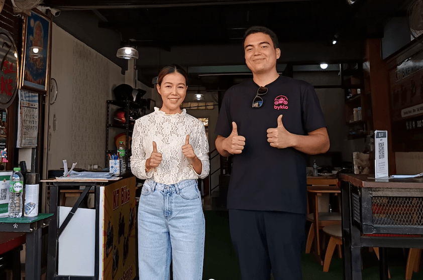 Two people standing outside motorbike rental shop in Chiang Mai. Byklo employee and owner of K7 Bike Chaing Mai giving thumbs up